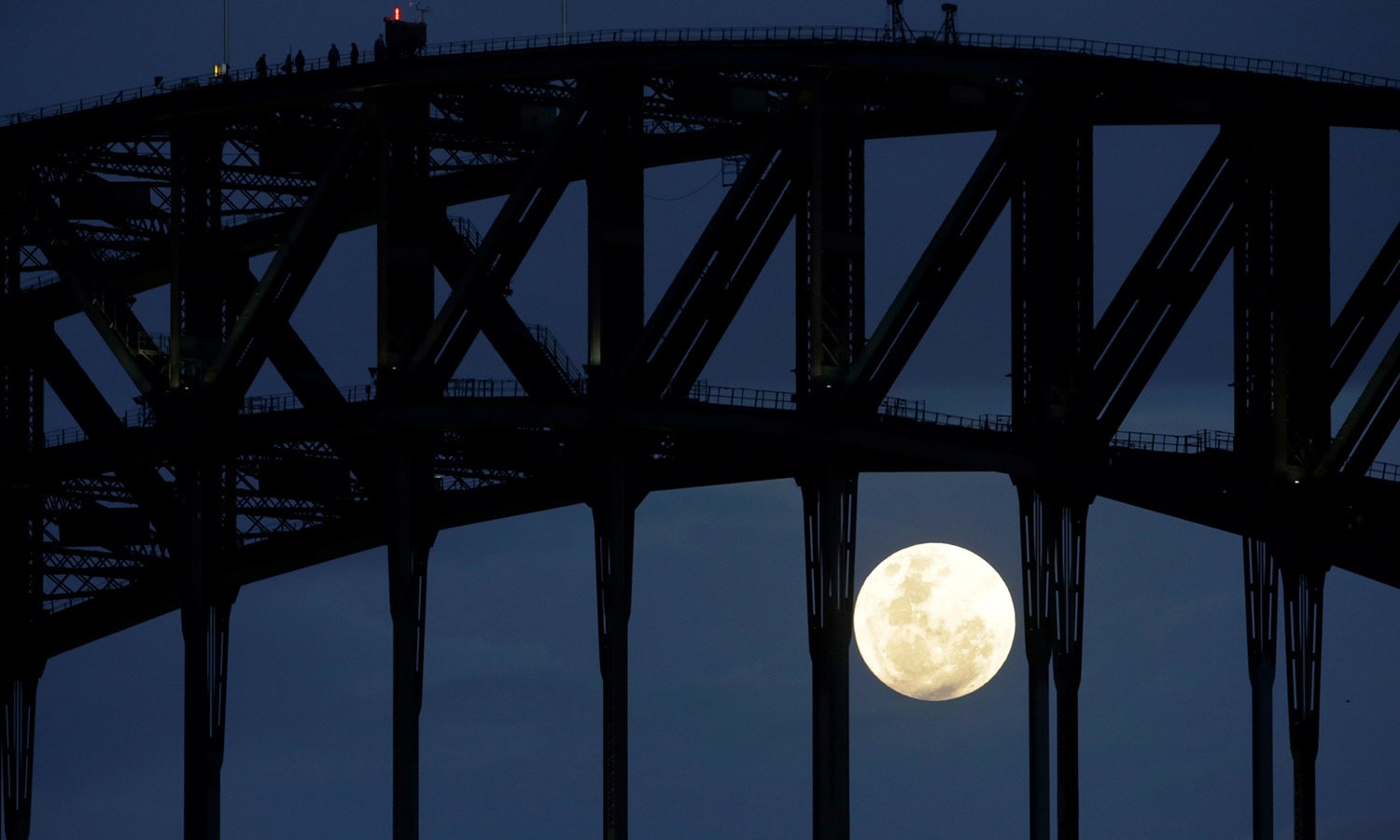 Participants in a Sydney Harbour Bridge Climb walk across the western span of the famous Australian landmark as the Super Moon rises after sunset