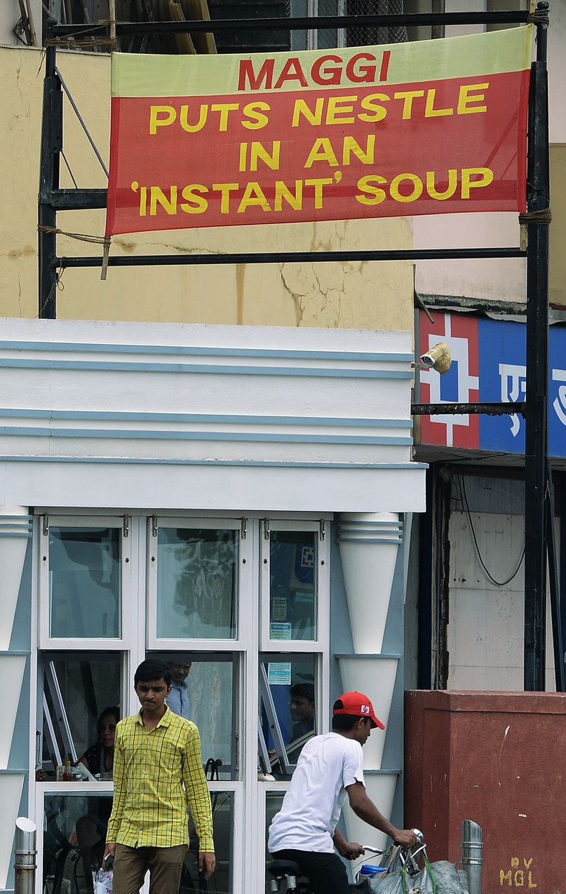 Indian commuters pass a banner bearing the name of the Maggi Nestle noodle brand in Mumbai on June 15, 2015. Nestle is challenging a ban imposed by India on its hugely popular Maggi instant noodles brand after tests showed they contained excessive levels of lead.  AFP PHOTO/ Indranil MUKHERJEE