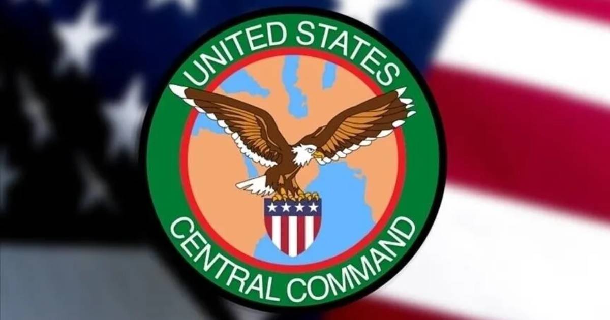 The official emblem of the United States Central Command (CENTCOM) set against a blurred American flag background. The emblem consists of a green circular ring with white text reading "UNITED STATES CENTRAL COMMAND." At its center, an American bald eagle with outstretched wings holds a patriotic red, white, and blue shield over a central map of the Middle East and Central Asia region.